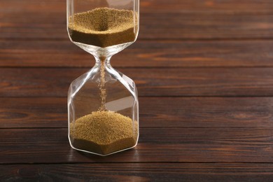 Hourglass with flowing sand on wooden table, closeup. Space for text