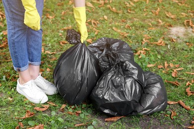 Photo of Woman holding plastic bags with garbage in park, closeup.