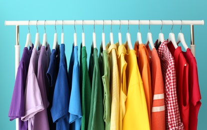 Rack with rainbow clothes on color background