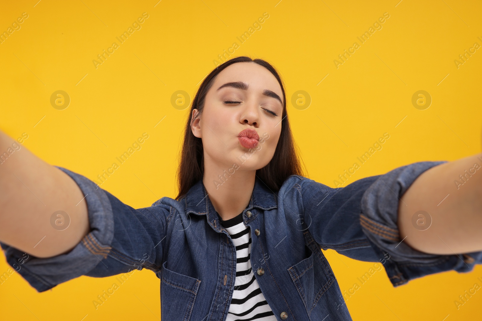 Photo of Young woman taking selfie and blowing kiss on yellow background