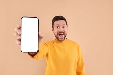 Surprised man showing smartphone in hand on light brown background