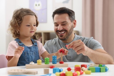 Photo of Motor skills development. Father and daughter playing with stacking and counting game at table indoors