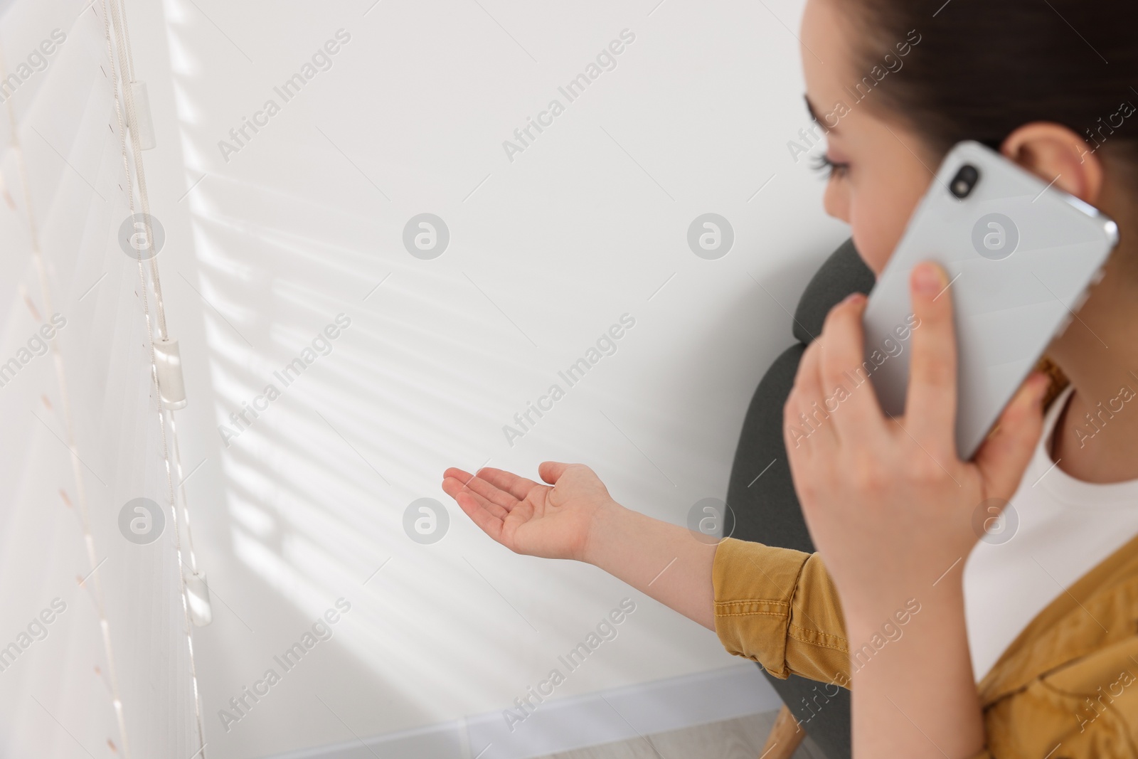 Photo of Woman talking on phone and pointing at white wall in room