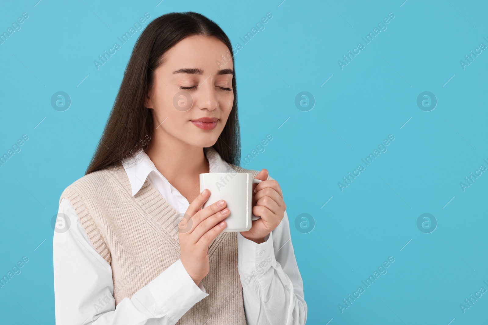 Photo of Beautiful young woman holding white ceramic mug on light blue background, space for text