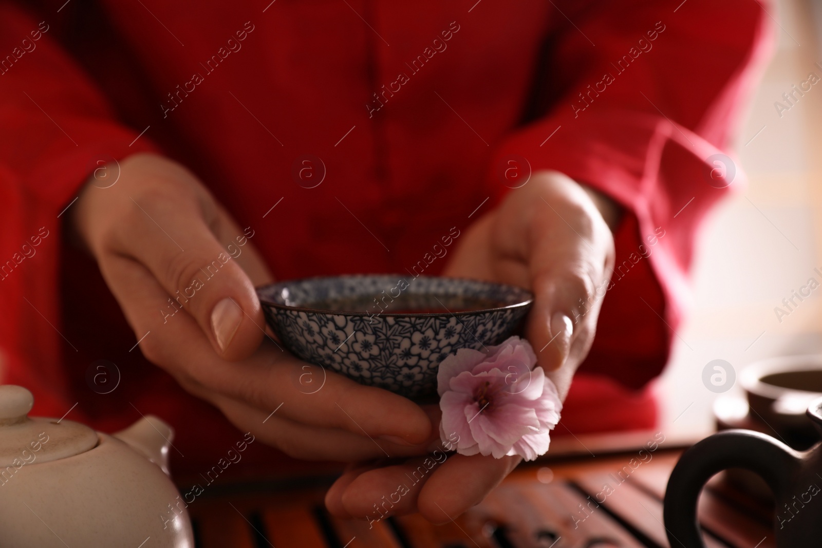 Photo of Master holding cup of freshly brewed tea and flower during traditional ceremony at table, closeup