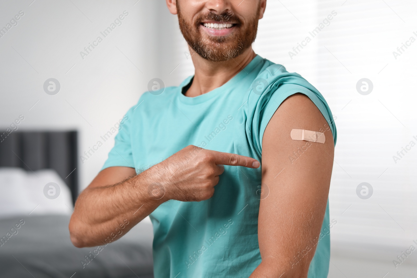 Photo of Man pointing at sticking plaster after vaccination on his arm in bedroom, closeup