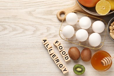 Food allergy. Different fresh products and cubes on light wooden table, flat lay with space for text