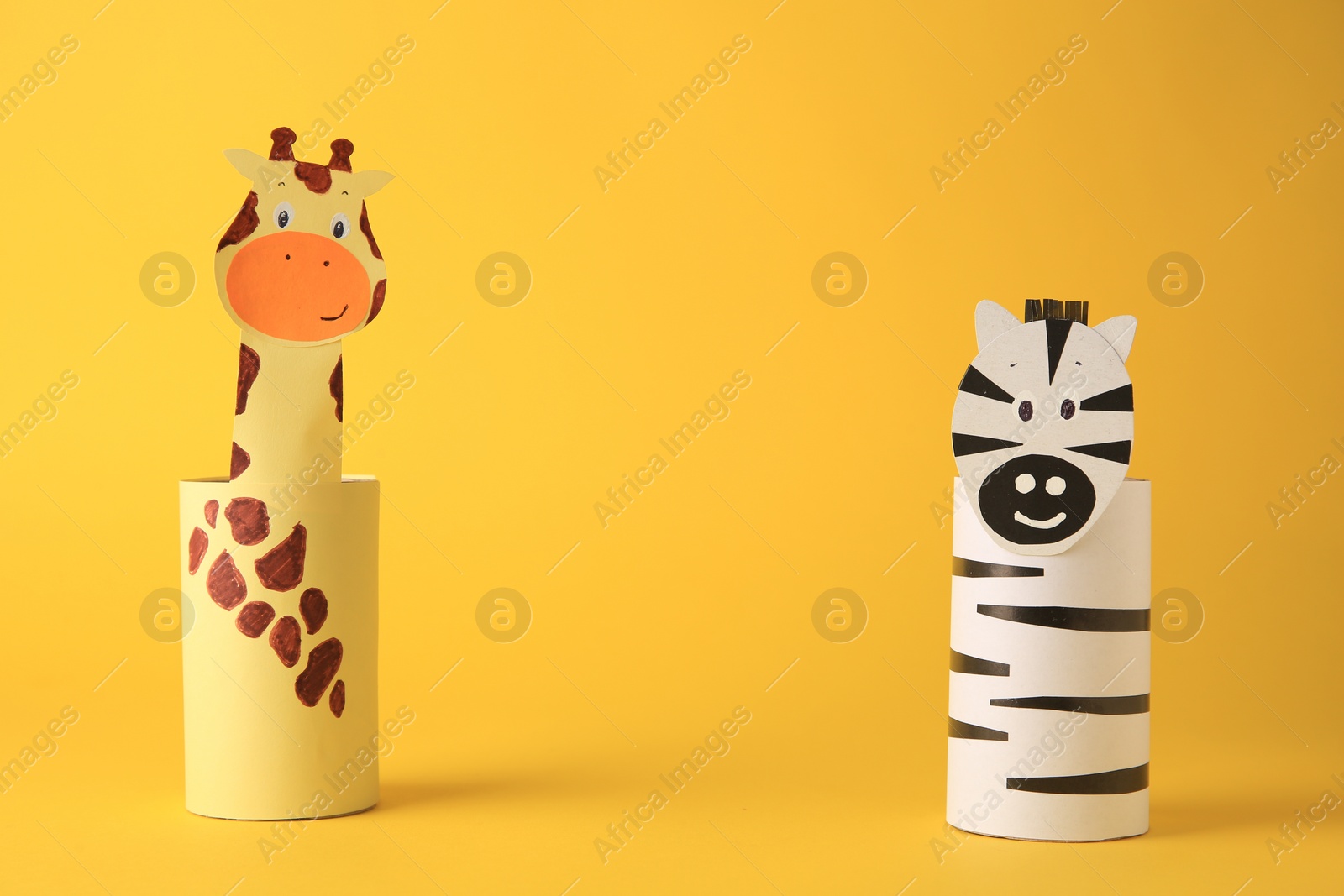 Photo of Toy giraffe and zebra made from toilet paper hubs on yellow background, space for text. Children's handmade ideas