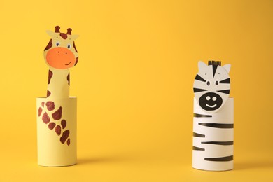 Photo of Toy giraffe and zebra made from toilet paper hubs on yellow background, space for text. Children's handmade ideas