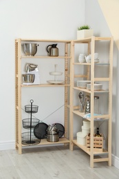 Photo of Wooden shelving units with kitchenware near color wall. Stylish room interior