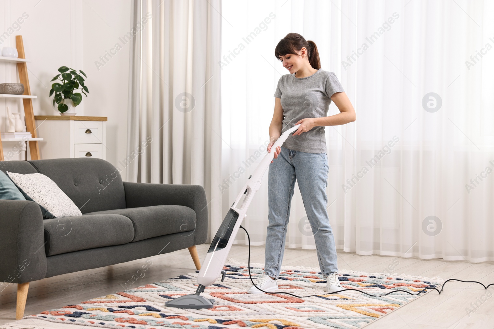 Photo of Happy young housewife vacuuming rug at home