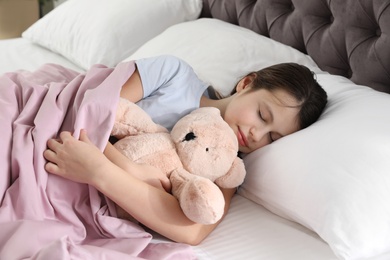 Photo of Beautiful little girl with teddy bear sleeping in bed