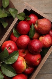Photo of Crate with wet red apples and green leaves on wooden table, top view