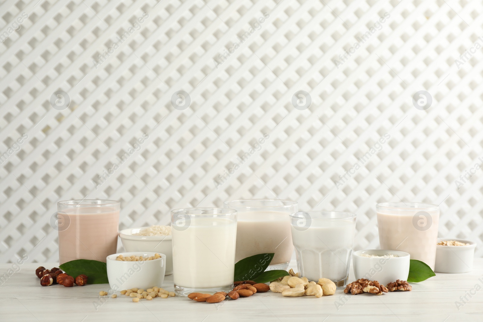 Photo of Different vegan milks and ingredients on white wooden table. Space for text