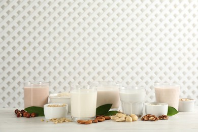 Different vegan milks and ingredients on white wooden table. Space for text
