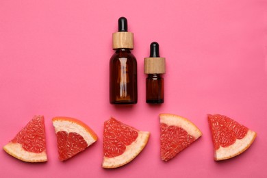 Photo of Bottles of citrus essential oil and fresh grapefruit slices on pink background, flat lay