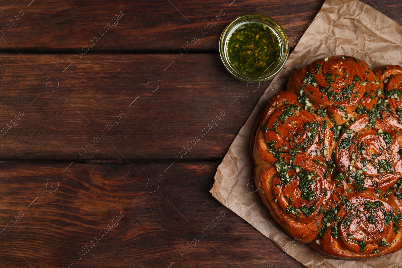 Photo of Traditional Ukrainian garlic bread with herbs (Pampushky) and aromatic oil on wooden table, flat lay. Space for text