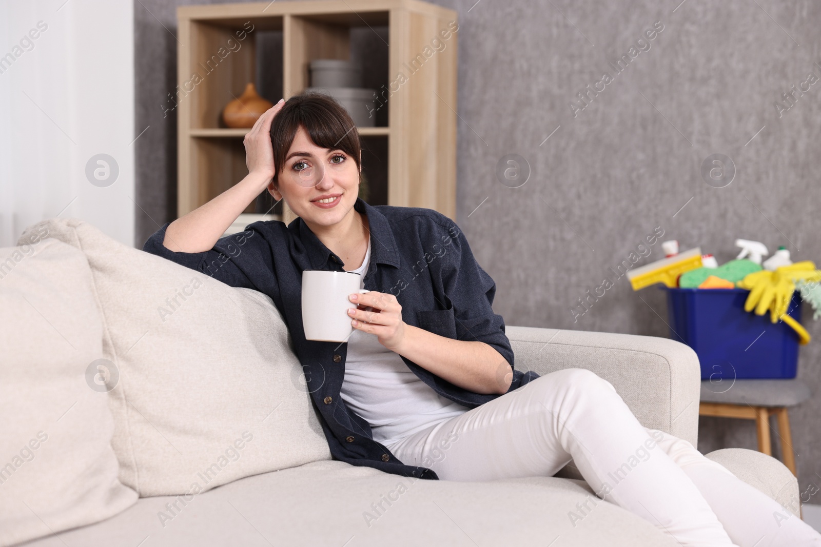 Photo of Beautiful young housewife with cup of drink resting after cleaning on sofa at home