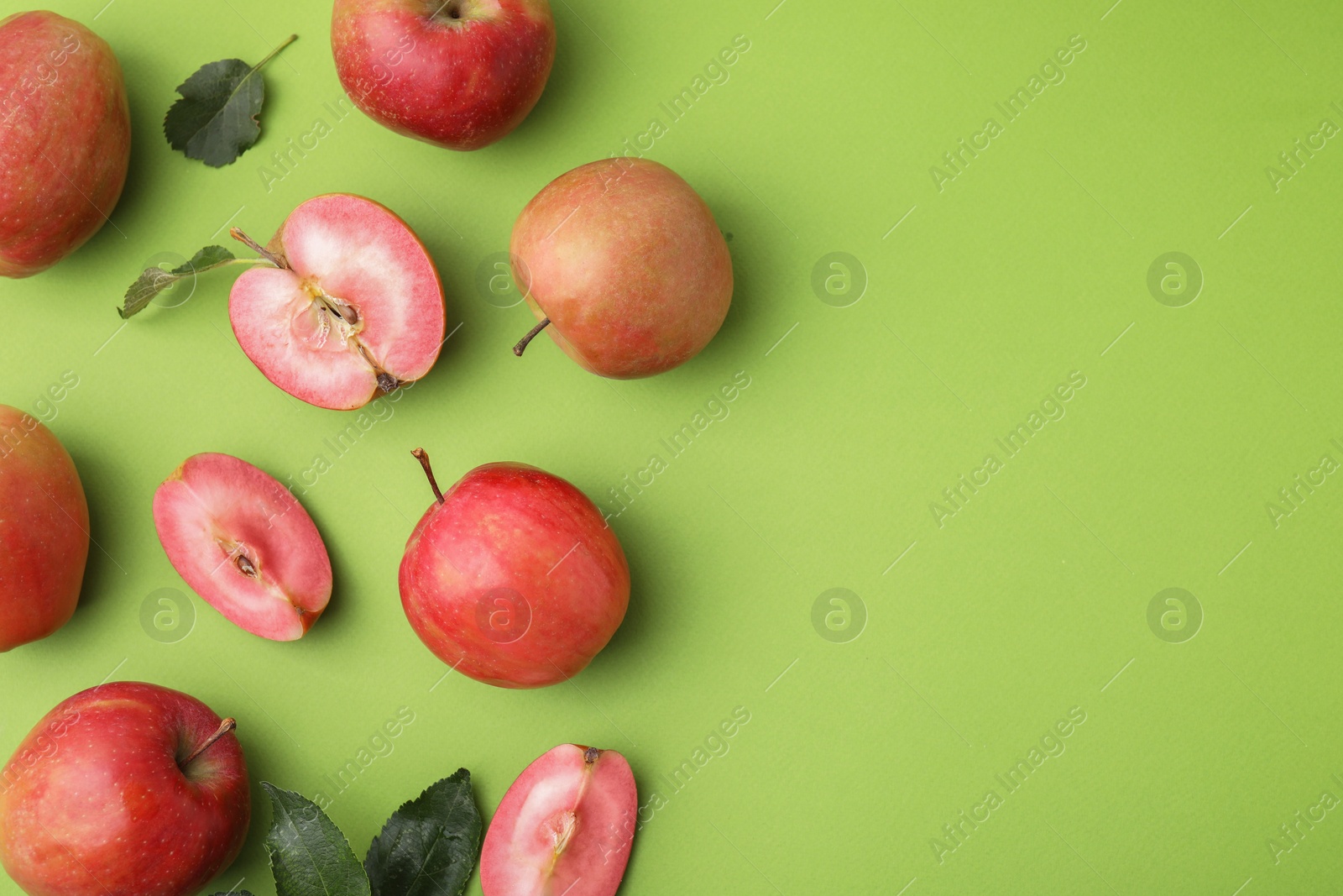 Photo of Tasty apples with red pulp and leaves on light green background, flat lay. Space for text