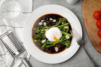 Photo of Tasty cooked broccolini with poached egg, almonds and sauce on grey table, flat lay