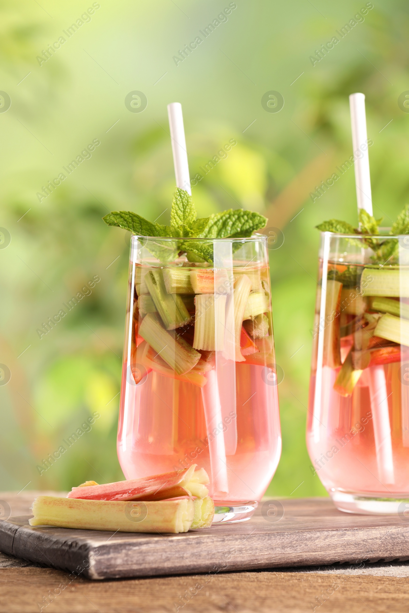 Photo of Glasses of tasty rhubarb cocktail on wooden table outdoors