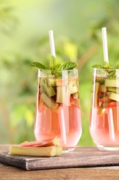 Glasses of tasty rhubarb cocktail on wooden table outdoors