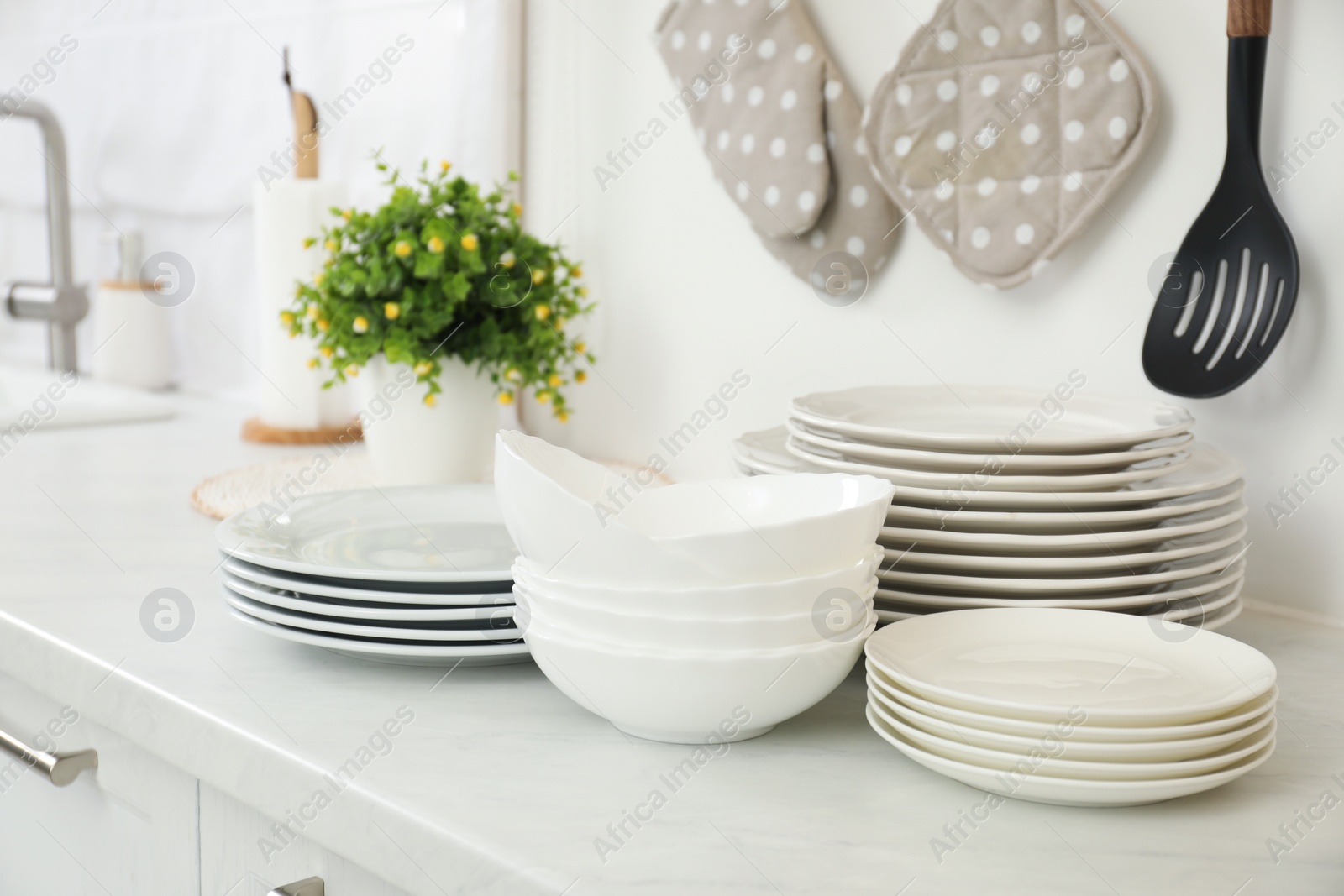 Photo of Clean plates and bowls on white marble countertop in kitchen