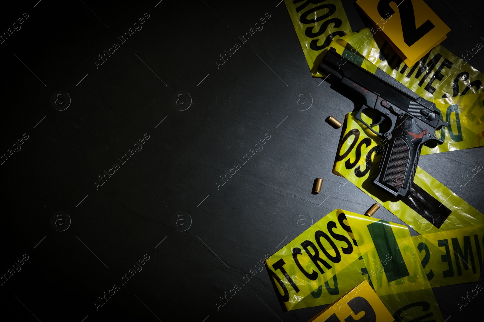 Photo of Flat lay composition with gun and crime scene tape on black slate background. Space for text