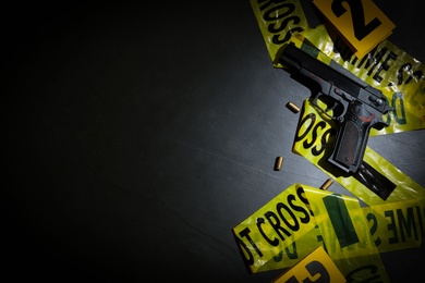 Photo of Flat lay composition with gun and crime scene tape on black slate background. Space for text