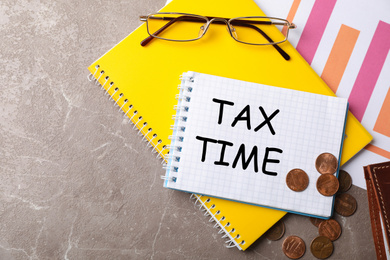 Flat lay composition with stationery, coins, glasses and words TAX TIME written in notebook on table