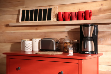 Photo of Modern coffeemaker and toaster on red chest of drawers near wooden wall