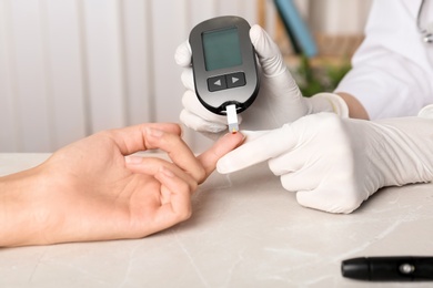 Doctor checking blood sugar level with glucometer at table. Diabetes test