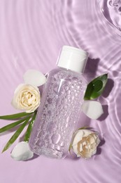 Flat lay composition with wet bottle of micellar water on violet background