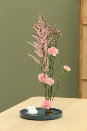 Photo of Stylish ikebana with beautiful pink flowers and burning scented candles carrying cozy atmosphere at home
