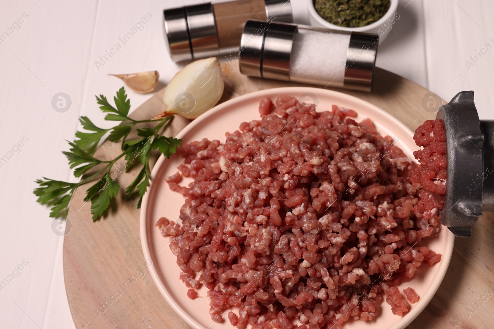 Photo of Manual meat grinder with beef mince, parsley, onion and spices on white wooden table, above view