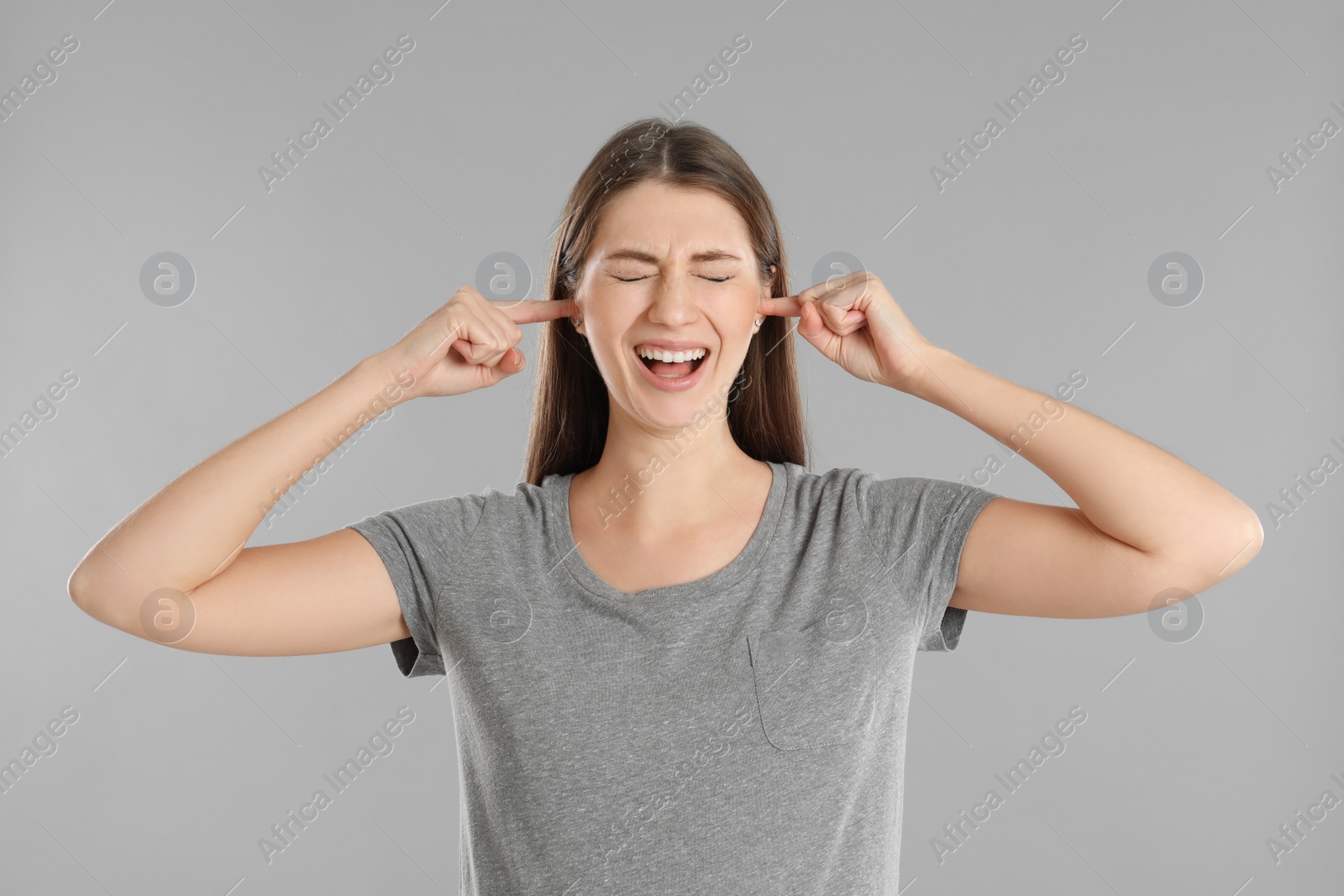 Photo of Emotional young woman covering her ears with fingers on grey background