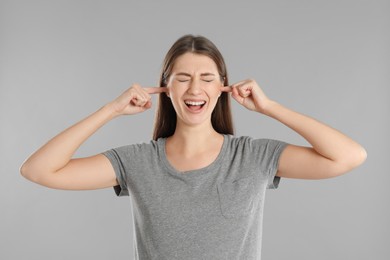 Photo of Emotional young woman covering her ears with fingers on grey background