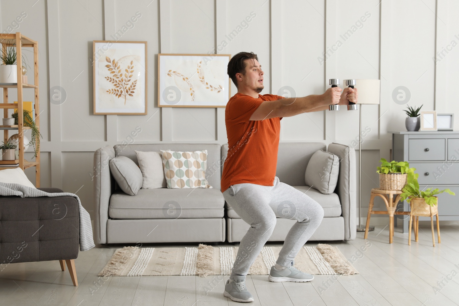 Photo of Overweight man doing squat exercise with dumbbells at home