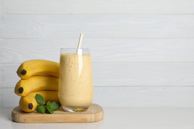 Photo of Glass of tasty smoothie, mint and fresh bananas on white wooden table. Space for text