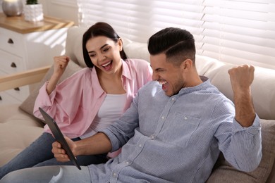 Photo of Emotional couple participating in online auction using tablet at home