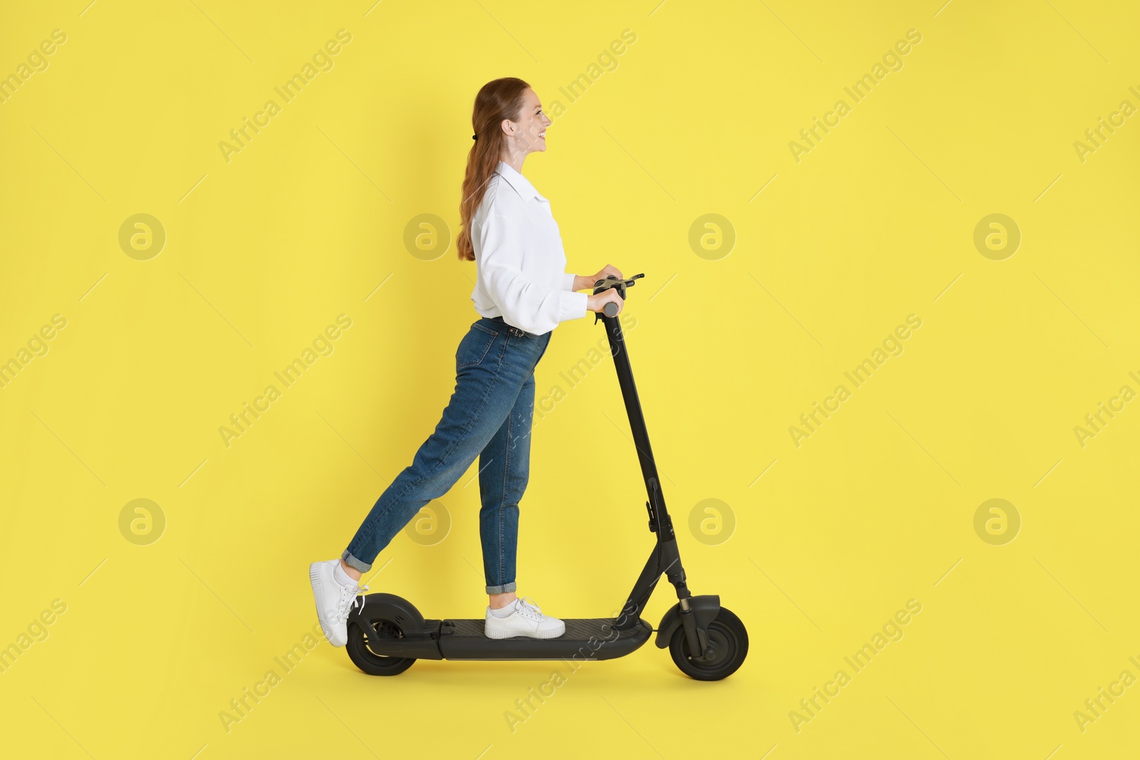 Photo of Happy woman riding modern electric kick scooter on yellow background