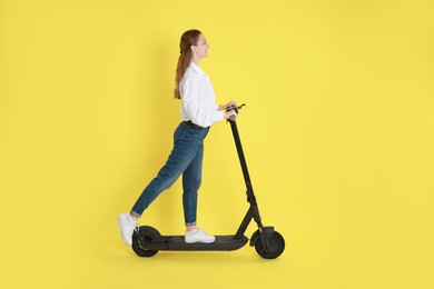 Happy woman riding modern electric kick scooter on yellow background