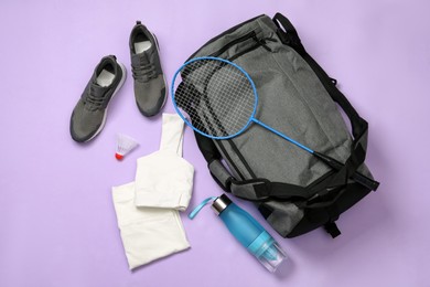 Grey sports bag and badminton equipment on violet background, flat lay