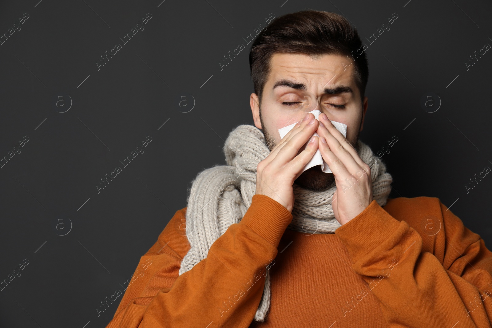 Photo of Handsome young man blowing nose against dark background. Space for text