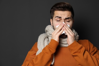 Handsome young man blowing nose against dark background. Space for text