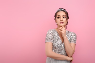 Beautiful young woman wearing luxurious tiara on pink background, space for text