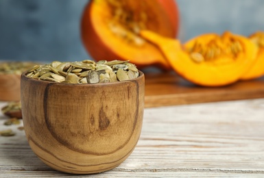 Photo of Bowl of raw pumpkin seeds on white wooden table. Space for text