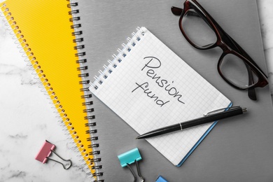 Flat lay composition with stationery, glasses and words PENSION FUND written in notebook on table