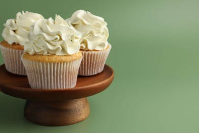 Photo of Tasty vanilla cupcakes with cream on green background, space for text