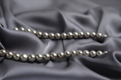 Photo of Beautiful silver pearls on grey silk, closeup